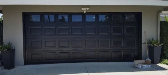 Black raised-panel garage door with matching dark trim on a light stucco home — black modern garage doors popular in Newport Beach, CA