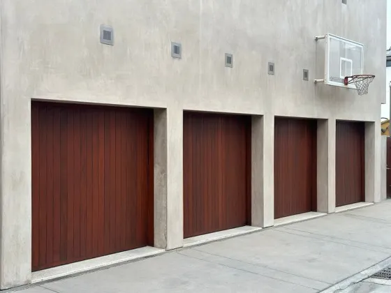 Row of four dark wood-look plank garage doors on a concrete building — door styles available through our Orange County installation service