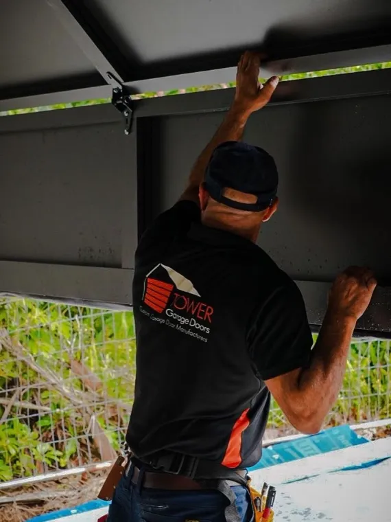 Technician working overhead on garage door safety hardware — sensor repair in Orange County