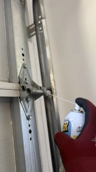 Technician lubricating garage door hinges and rollers during a maintenance tune-up in Laguna Hills, CA